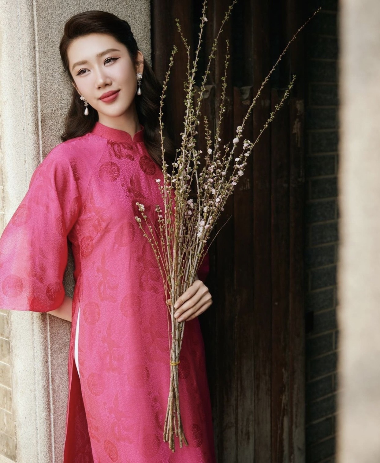 Thúy Ngân mặc áo dài hồng tay lửng, đeo bông tai ngọc trai, tô son hồng đậm và chải tóc uốn lượn cổ điển.