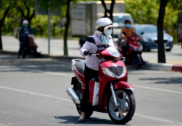 Người phụ nữ đứng giữa trời nắng đợi đèn xanh trên đường Mai Chí Thọ, quận 2, trong khi một số người khác đậu theo mép đường có cây xanh.