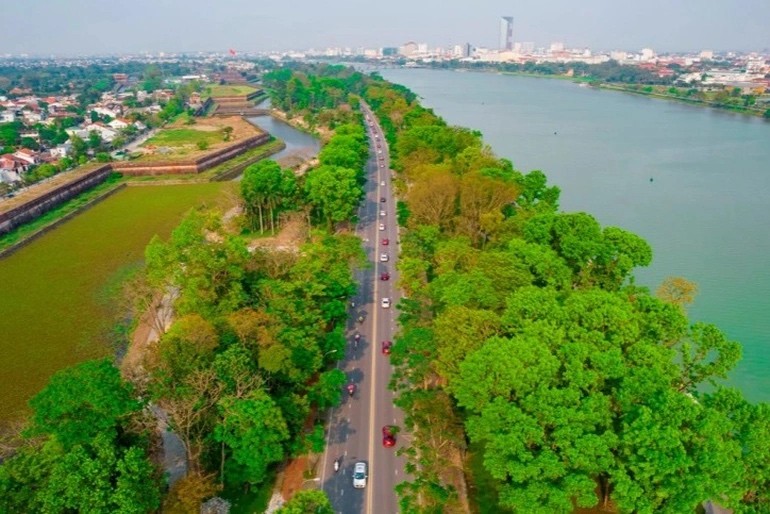 Đoàn xe đi vào Huế trên trục đường Lê Duẩn với một bên là sông Hương và một bên là các đền đài di tích.