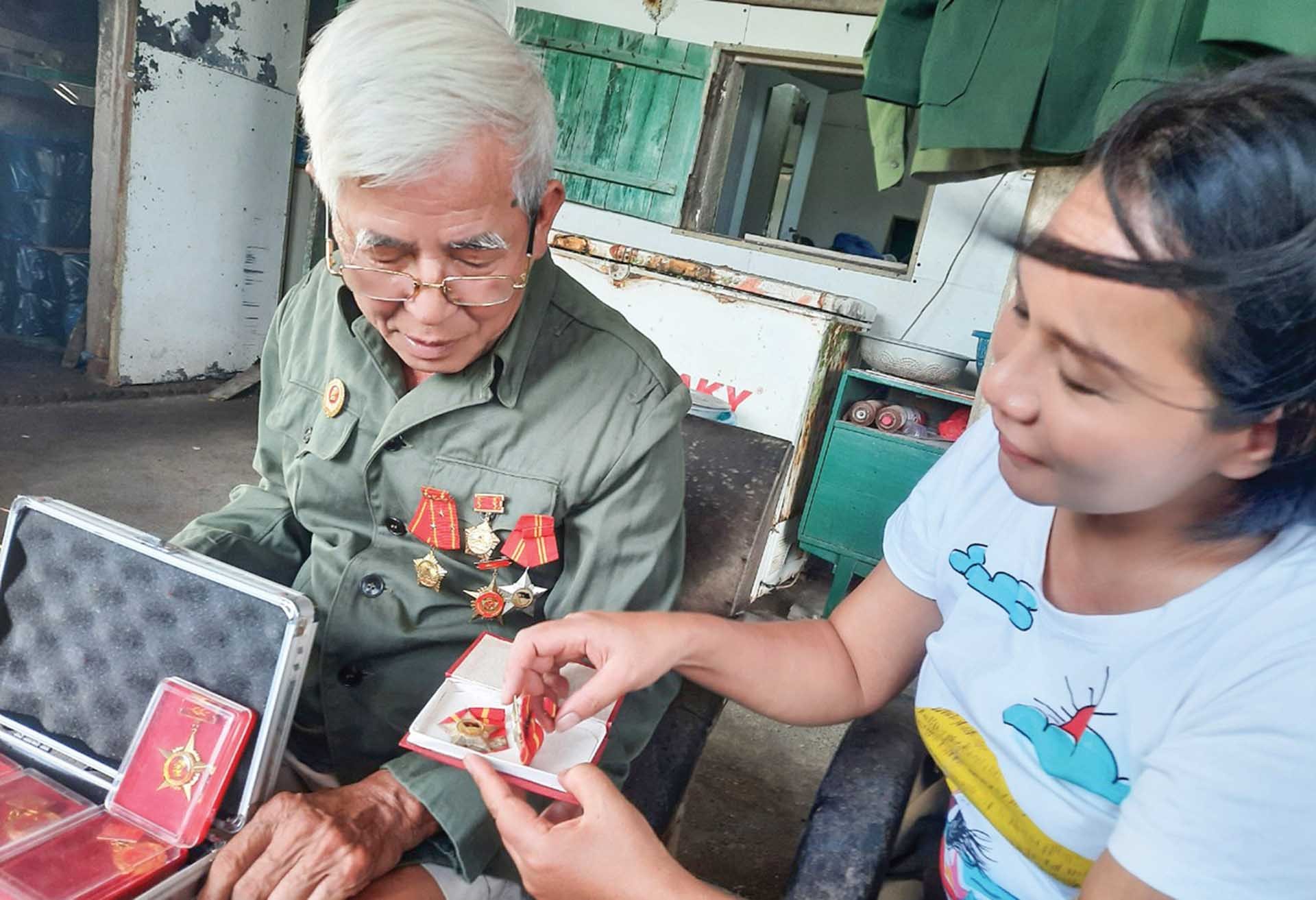 Tác giả và nhân vật bên những kỷ vật những huân huy chương được Đảng và Nhà nước trao tặng. (Ảnh: Hạnh Mi) Tác giả và nhân vật bên những kỷ vật những huân huy chương được Đảng và Nhà nước trao tặng. (Ảnh: Hạnh Mi)