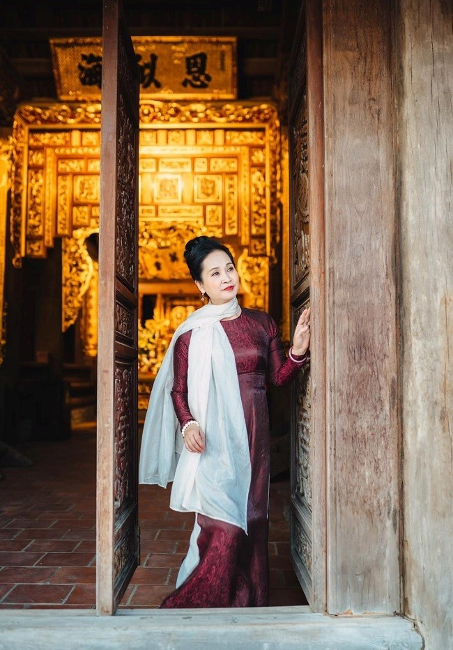 NSND Lan Hương dịu dàng trong mẫu áo dài đỏ in hoa văn kết hợp cùng quần trắng và khăn quàng tone-sur-tone. Chiếc khăn voan vắt ngang vai là điểm nhấn giúp nữ nghệ sĩ thêm đài các, cùng kiểu tóc búi cao tôn lên đường nét gương mặt.